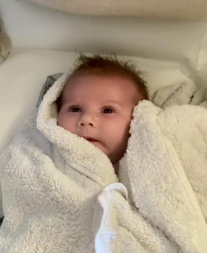 Nyfödd bebis i mjuk handduk, lugn och nyfiken blick.