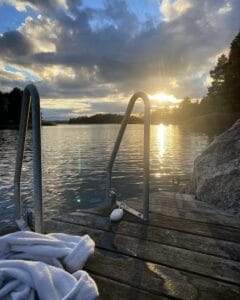 Litet trädäck med stege vid sjöns kant under solnedgången.